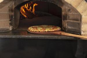 Brazilian pizza is cooked in a wood-fired oven. Pizza cooking in a traditional brick wood oven. Brick oven pizza on the wooden holder going to bake. photo