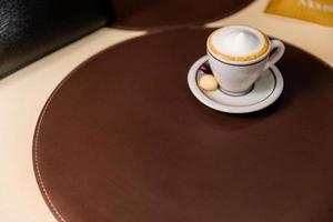 Cappuccino with nice frothy foam. Latte art with a heart made from milk. Coffee cup with a saucer and a teaspoon on a table.
