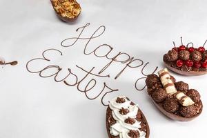 Happy Easter written with melted chocolate on white background. With gourmet Easter eggs decorating on the sides.
