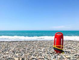 Red rescue float on rocky beach with sea panorama and no lifeguard. Static blank space copypaste background safety concept photo