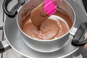 Cooking pot with chocolate melting being removed by chef hand on the stove of a kitchen to make sweet desserts. Bulk chocolate melting in a pot.