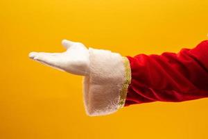 Close-up of Santa Claus gloved hand show giving gesturing on yellow background. Festive time for happy New Year, Merry Christmas, traditional seasonal celebration. photo