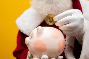 santa claus poniendo monedas en una alcancía de cerámica. concepto de ahorro para fin de año. gastar en navidad. gastado en regalos de navidad. foto