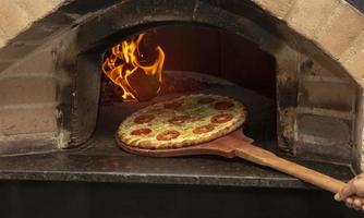 Brazilian pizza is cooked in a wood-fired oven. Pizza cooking in a traditional brick wood oven. Brick oven pizza on the wooden holder going to bake. photo