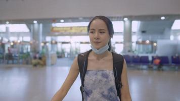 jeune jolie femme asiatique portant un masque médical de protection marchant à l'intérieur du terminal de l'aéroport, le passager monte sur l'escalator pendant la pandémie du virus corona covid19, concept de distanciation du voyageur en sac à dos