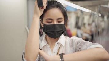 Asian female looking at time, wear face mask, holding handle standing inside metro subway train, rush hour, covid-19 new normal, protection on public transport, social distancing, infectious disease