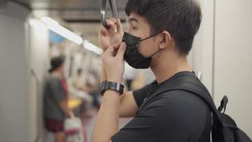 asiatischer mann passt schwarze schutzmaske an, während er in der u-bahn steht, hauptverkehrszeit pendeln auf bahnfahrt, covid-19 neue normalität, schutz in öffentlichen verkehrsmitteln, soziale distanzierung, ansteckende krankheit video