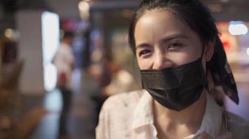 Attractive Asian young woman looking at camera smile under face mask, happy life fun and friendly female, covid-19, social distancing concept, New normal lifestyle, positive thinking, blur background video