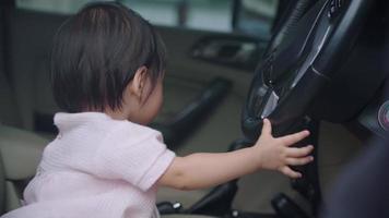 bambino asiatico che gioca con il volante dell'auto con curiosità, finge di guidare un'auto, siediti sul sedile del conducente, innocenza infantile, esperienza di apprendimento, sviluppo felice e gioioso dei bambini, viaggio in sicurezza con il bambino video