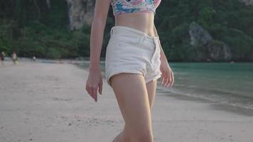 ung attraktiv asiatisk kvinna i strandkläder tycker om att gå längs stranden, snäckskalsinsamlingsaktivitet, sitta med händerna och gräva hål på ren strand på sommarlovet, sexig tjej i bikini