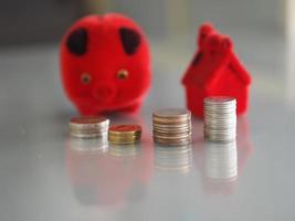 Many coins are stacked rows orderly reflection on blurred background and red pig coin bank, piggy bank, money box and red model house photo