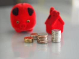 Many coins are stacked rows orderly reflection on blurred background and red pig coin bank, piggy bank, money box and red model house photo