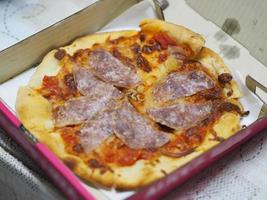 salami de pizza encima de salchicha seca con salsa de pizza y queso en caja de papel, fondo de comida foto