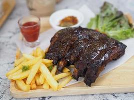 Pork Spareribs BBQ, Barbeque Pork Ribs with french fries vegetable salad, tomato sauce in a clear glass on wooden tray, food
