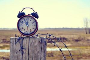 Old retro alarm clock on post tied with barbed wire symbolizes arrival of spring. photo