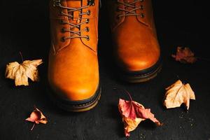 Brown autumn boots on a black background with scattered maple leaves.