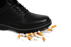 el zapato negro aplasta los cigarrillos sobre un fondo blanco.negación de fumar. foto