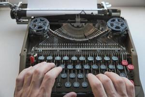 los dedos escriben texto en el teclado de una vieja máquina de escribir mecánica retro. foto