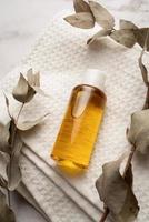 maqueta de botella de aceite esencial, botella de plástico con producto cosmético en toallas de baño blancas y hojas de eucalipto foto