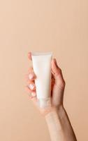 Face cream Mock-Up. Female hand holding white cream tube on beige background photo