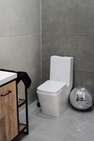 toilet and small washbasin in simple bathroom in gray floor and wall tiles photo