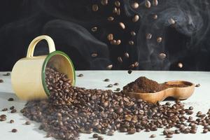 Taza de café y frijoles y café molido en un recipiente de madera sobre un fondo blanco.