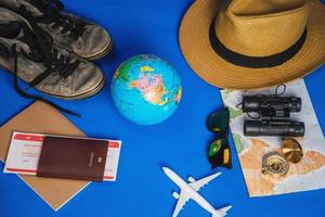 vacaciones de planificación turística con la ayuda del mapa mundial con otros accesorios de viaje. teléfono inteligente, cámara de cine y gafas de sol sobre un fondo azul. mochila de viaje foto