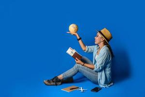 joven viajero asiático feliz con camisa azul con pasaporte con el mundo de la pelota en la mano. viaje conceptual con equipo para vacaciones de viajeros, sobre fondo de color azul. viajar relajarse foto