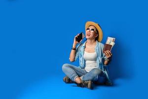 Traveler girl in a blue dress is smiling happy with a cheerful face and holding passport with holding mobile phones in the hand, on blue color background. concept travel photo