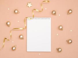 Christmas and new year card, or mock up on a pink peach background. Empty blank Notepad and small Golden balls, space for text. photo