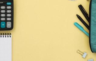 vista superior de un escritorio con una caja de lápices, bolígrafos, bloc de notas y calculadora sobre un fondo amarillo. concepto creativo con regreso a la escuela. disposición plana de elementos con espacio para texto. foto