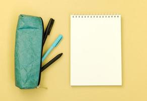 Top view of a Desk with a pencil case and an empty Notepad on a yellow background. Flat lay of items with space for text. photo