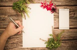 espacio conceptual para texto, que consiste en el mango de un bolígrafo y escritura móvil en un papel en blanco, azalea y flores de albahaca sobre un fondo de madera. vista superior. plano foto