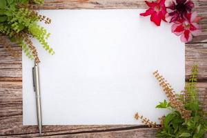 Conceptual space for text, which consists of blank paper, azalea, basil flowers,and pens on a wooden background.Blank template for your text.top view.flat lay