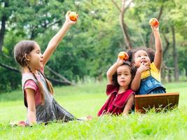 A group of young children of many nationalities play and eating fruits outside of school photo