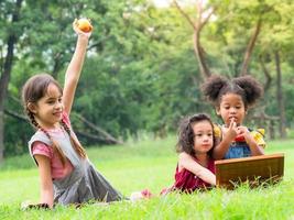 un grupo de niños pequeños de muchas nacionalidades juegan y comen frutas fuera de la escuela foto