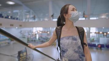 viajera asiática usa mascarilla protectora parada en una escalera mecánica con mochila dentro de una terminal de aeropuerto vacía, enfermedades infecciosas en lugares públicos higiene, nueva pandemia normal, seguro de viaje video