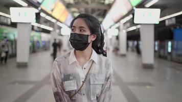 Asian female wear black mask standing and looking at camera in sky train station, covid, woman inside subway station, New normal lifestyle, self protection, public transportation, evening white light