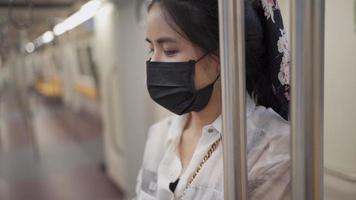 une jeune femme asiatique porte un masque facial noir, debout à l'intérieur d'une rame de métro, nouveau mode de vie à distance sociale normale, autoprotection, voiture de métro vide, ralenti contagieux, risque de transport en commun video