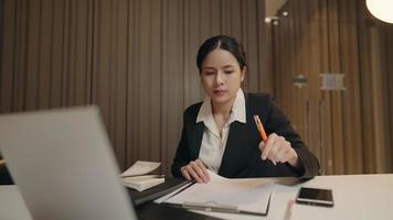 Asian concentrated young entrepreneur woman in formalwear late working alone at office room. Closeup focused executive CEO signing report after checking information. business and succession