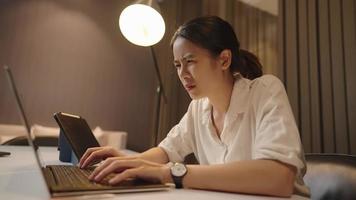 Aziatische vrouwelijke universiteitsstudent die tot laat in de nacht onderzoek doet en op haar scriptie schrijft, haastwerk voor de komende deadline, zich uitgeput en vermoeiend voelen, middernachtstudie met laptopcomputer