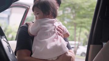 Asian young adult father placing playing his baby girl on the  driver seat inside the car, baby playing with steering wheeling pretending to drive on family trip, Family member Happiness bonding video