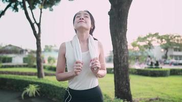 jonge aantrekkelijke aziatische vrouwen ademen vers voordat ze buiten joggen of rennen met een groene parkachtergrond, terwijl de zon ondergaat in de zomer, concept gezond hardlopen en buitenoefening video