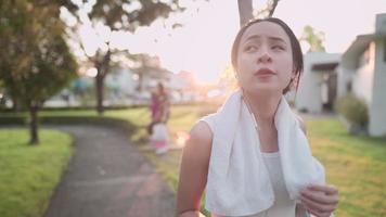 mujer joven asiática caminando en el parque después del entrenamiento, bienestar físico de la vida, automotivación, plan de seguro de vida, estilo de vida saludable, con la luz del atardecer detrás, actitud positiva felicidad despreocupada video