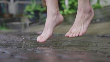 após a atividade de chuva, feche os pés descalços lentamente pisando em poças de água em uma calçada de cimento, estação chuvosa tropical, mudanças climáticas, questão ambiental, adulto se divertindo jogando água video