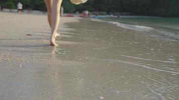 a seguir tiro em uma mulher confiante pernas descalças andando segurando um chapéu de sol ao longo de uma praia lotada nas férias de verão, recursos naturais da ásia, atividade de praia, com uma equipe de canoagem localizada atrás video