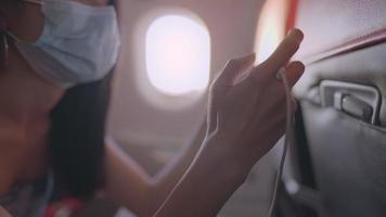 mujer asiática usa una máscara médica protectora usando el teléfono, descansando en el asiento del avión, a bordo del avión, entretenimiento a bordo, transporte público riesgo de enfermedades infecciosas, pandemia de covid video