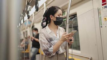 donna asiatica in maschera protettiva nera utilizzando smartphone, stare in piedi appoggiato al palo, covid-19 nuova normalità, donna in metropolitana, autoprotezione sui mezzi pubblici, distanza sociale, smarrimento video