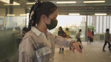 jonge aziatische vrouw draagt een zwart beschermend masker dat staat en kijkt naar de tijd in het metrostation. covid-19 dame wacht op vrienden, afspraak ontmoeten, zelfbescherming in het openbaar vervoer, gouden zonsondergang video