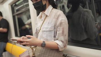joven mujer asiática enviando mensajes de texto en un teléfono inteligente dentro del metro, covid-19, comunicación de transporte público, distanciamiento social, nueva normalidad, conexión de red 4g 5g tecnología inalámbrica, estilo de vida de la ciudad